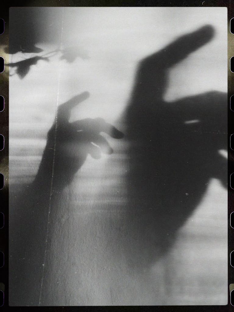 Black and white shadow play with hands creating abstract eerie shapes on a light background.